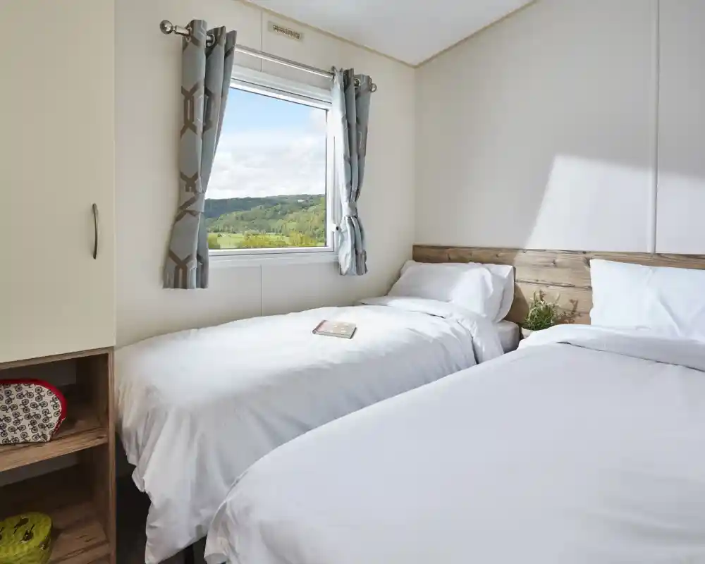 Bedroom with two twin beds, white bedding, patterned curtains, and a window overlooking a green landscape.