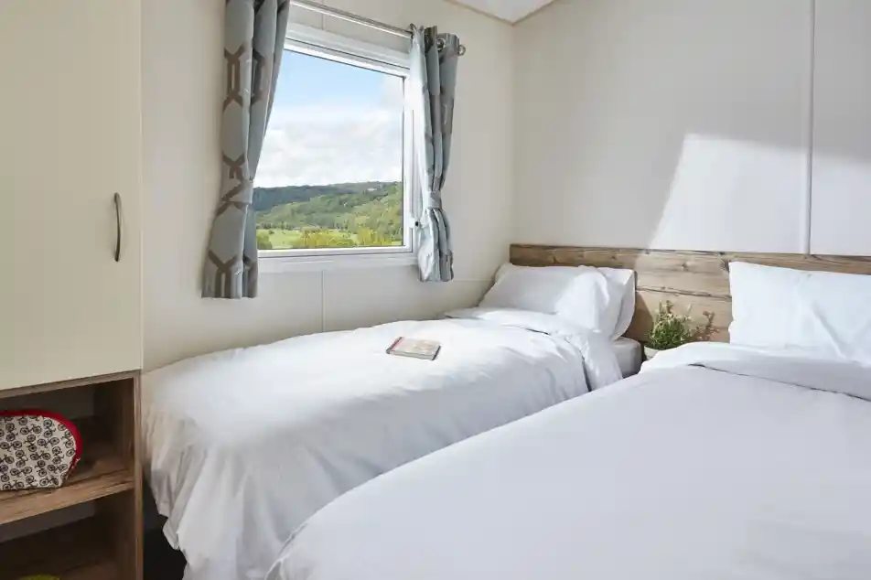 Bedroom with two twin beds, white bedding, patterned curtains, and a window overlooking a green landscape.