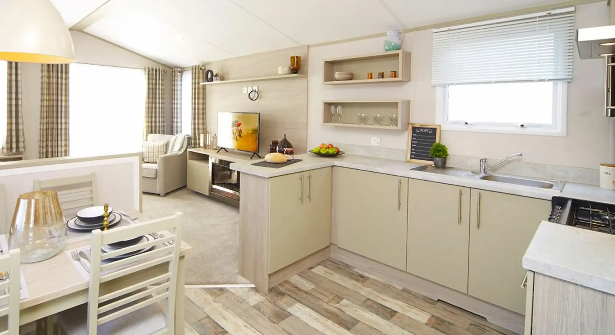 Modern mobile home interior featuring bright kitchen, dining area and living room with a TV.