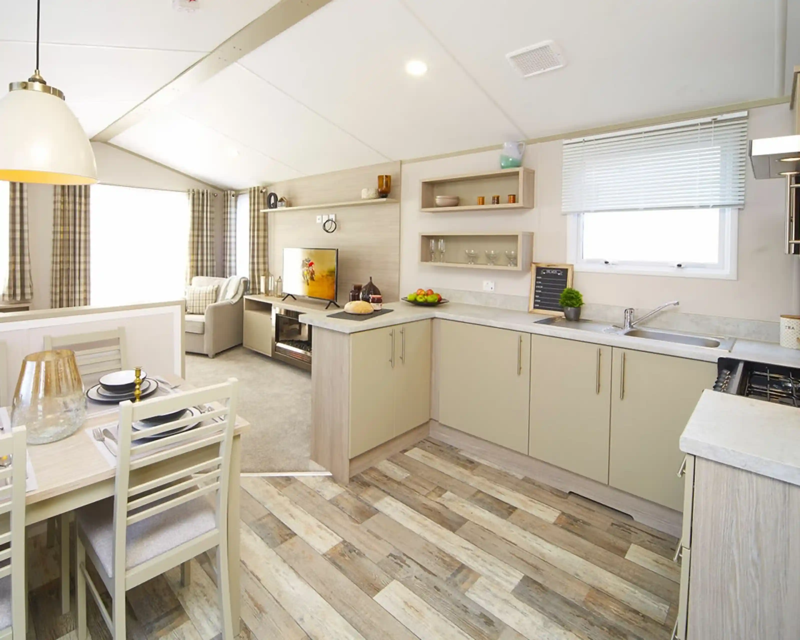 Modern mobile home interior featuring bright kitchen, dining area and living room with a TV.