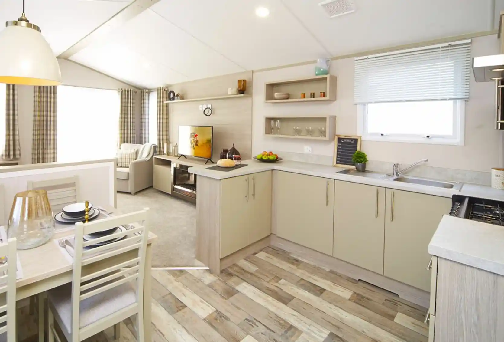 Modern mobile home interior featuring bright kitchen, dining area and living room with a TV.