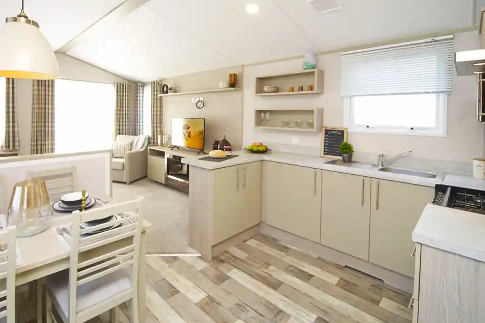 Modern mobile home interior featuring bright kitchen, dining area and living room with a TV.