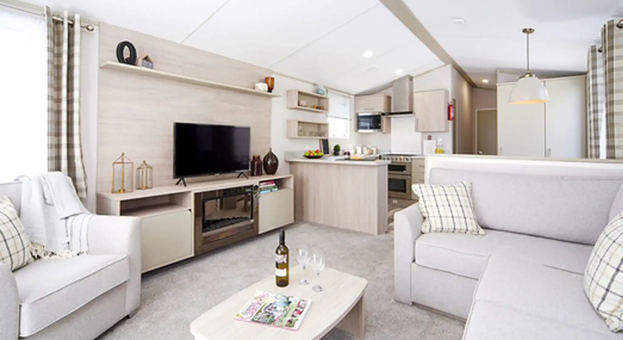 Modern living room and kitchen area with light grey sofas, a TV stand with a black television, and a neutral-toned kitchen with appliances.