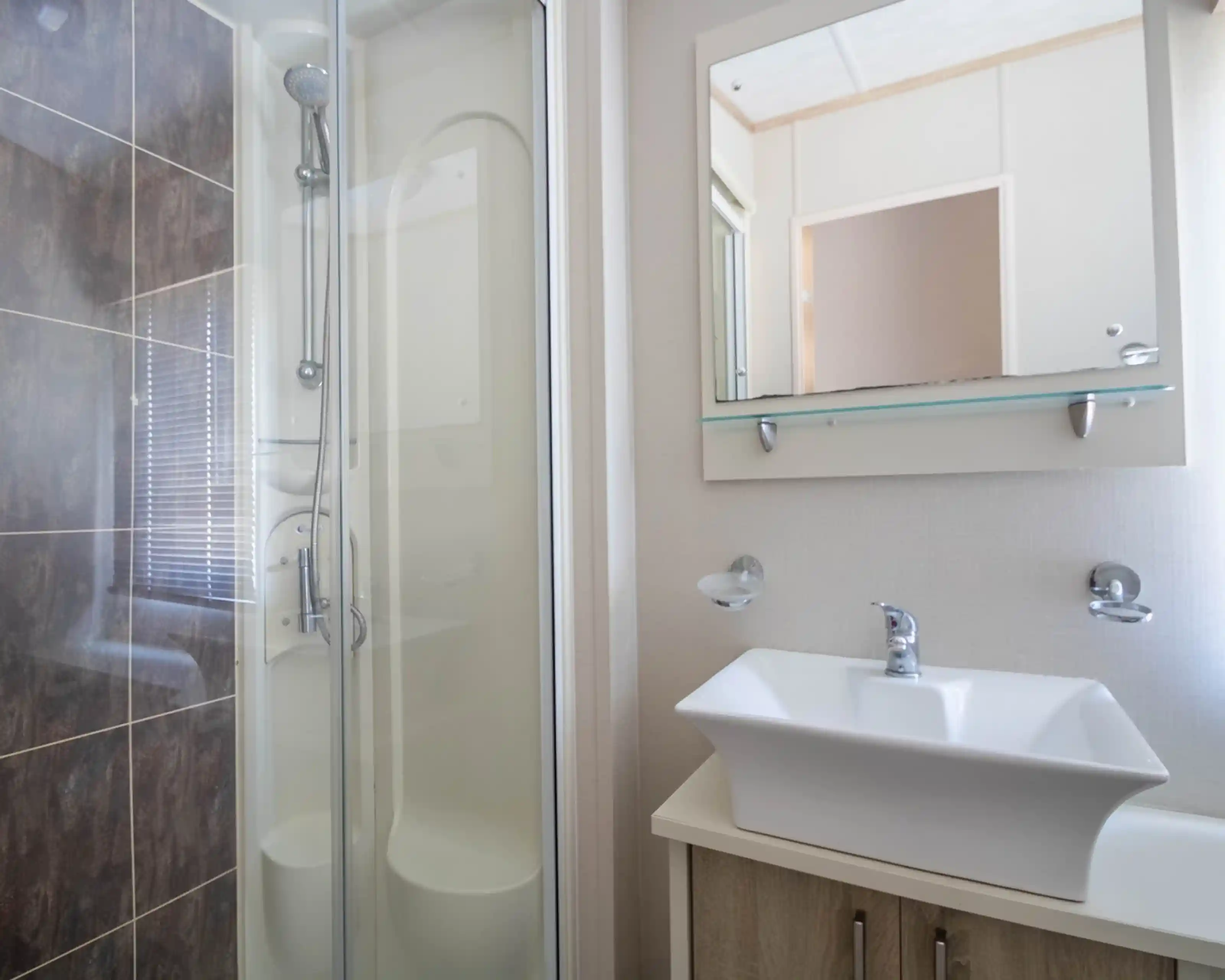 A modern bathroom featuring a glass shower stall, a stylish sink with a sleek faucet, and minimalistic wall decor. Natural light filters through a window.