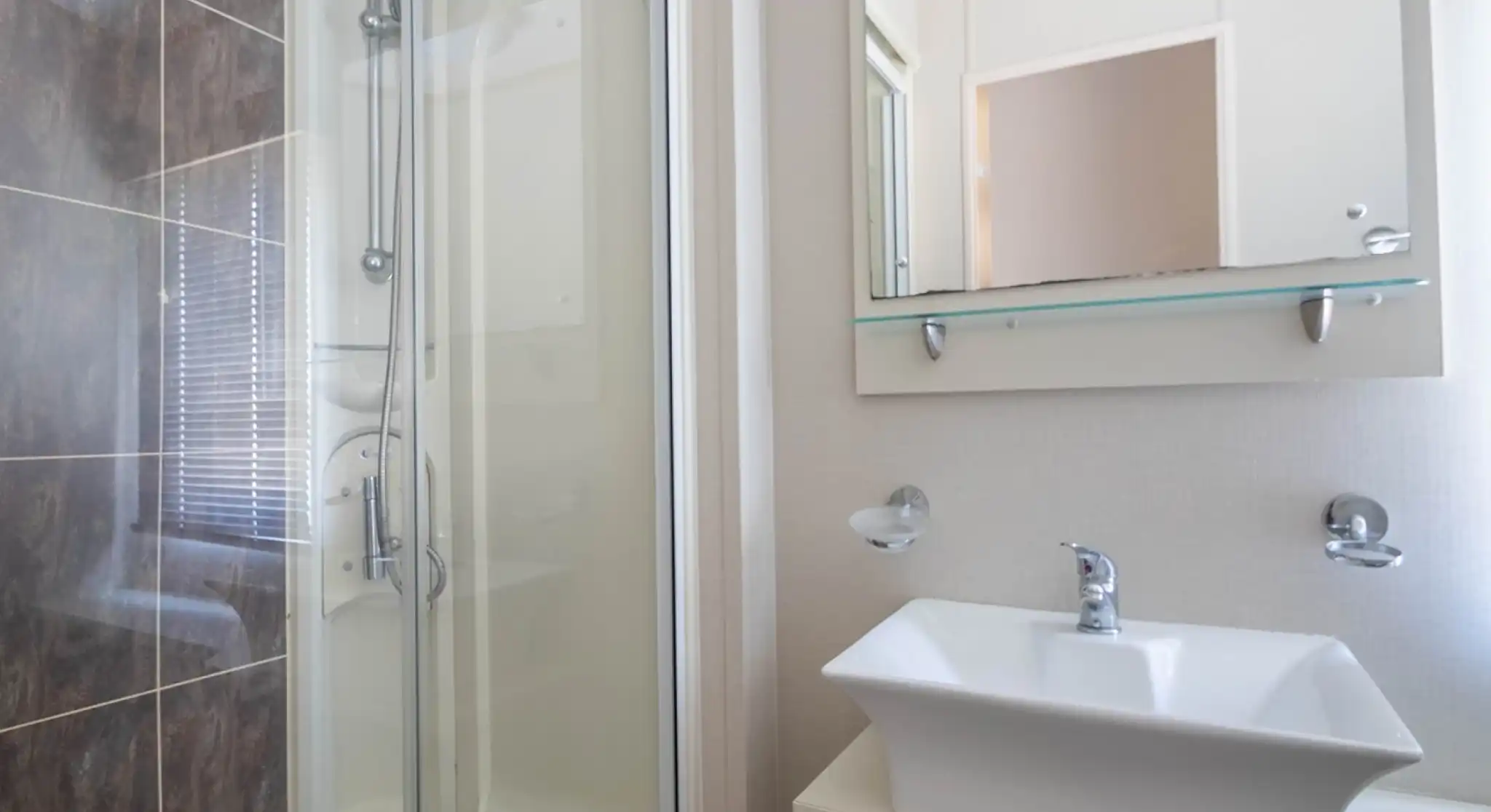 A modern bathroom featuring a glass shower stall, a stylish sink with a sleek faucet, and minimalistic wall decor. Natural light filters through a window.