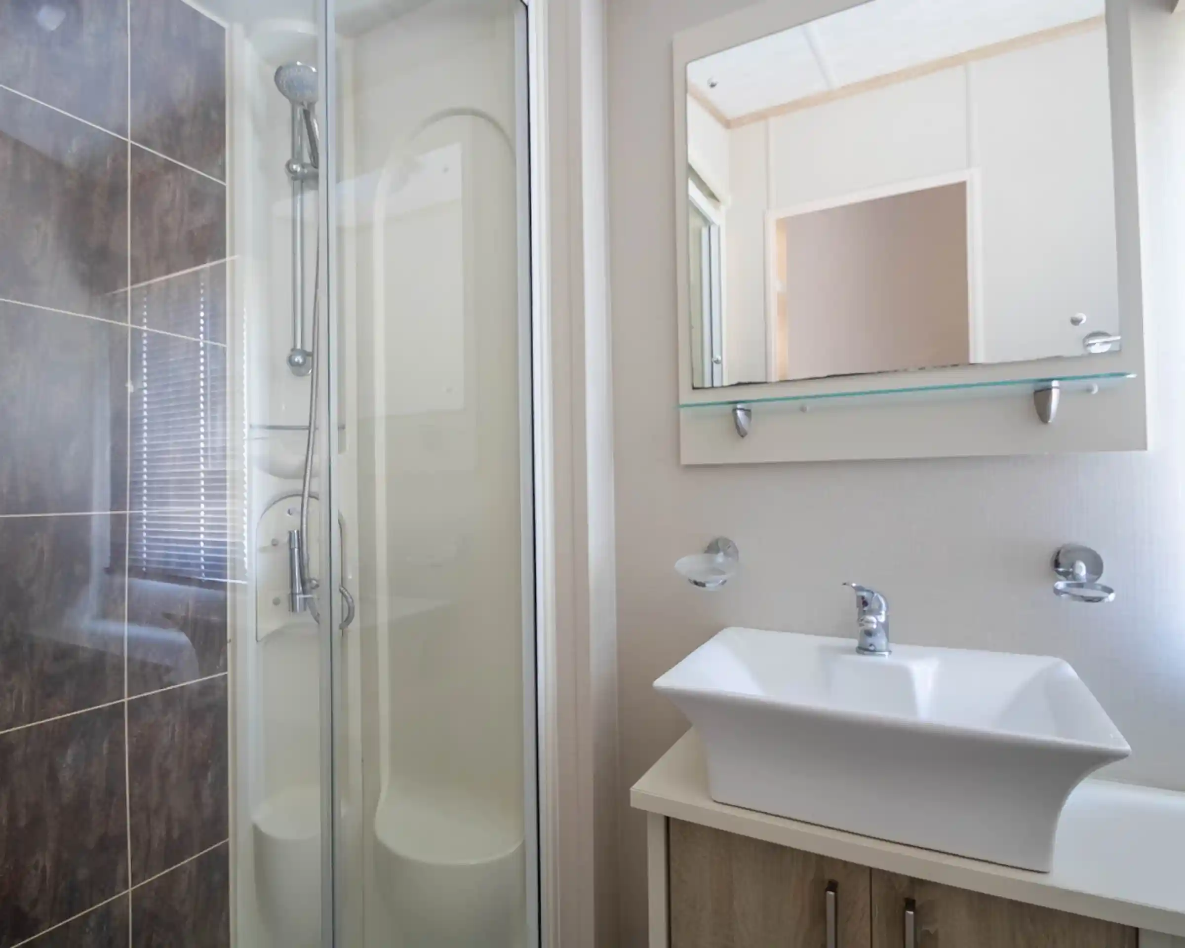 A modern bathroom featuring a glass shower stall, a stylish sink with a sleek faucet, and minimalistic wall decor. Natural light filters through a window.