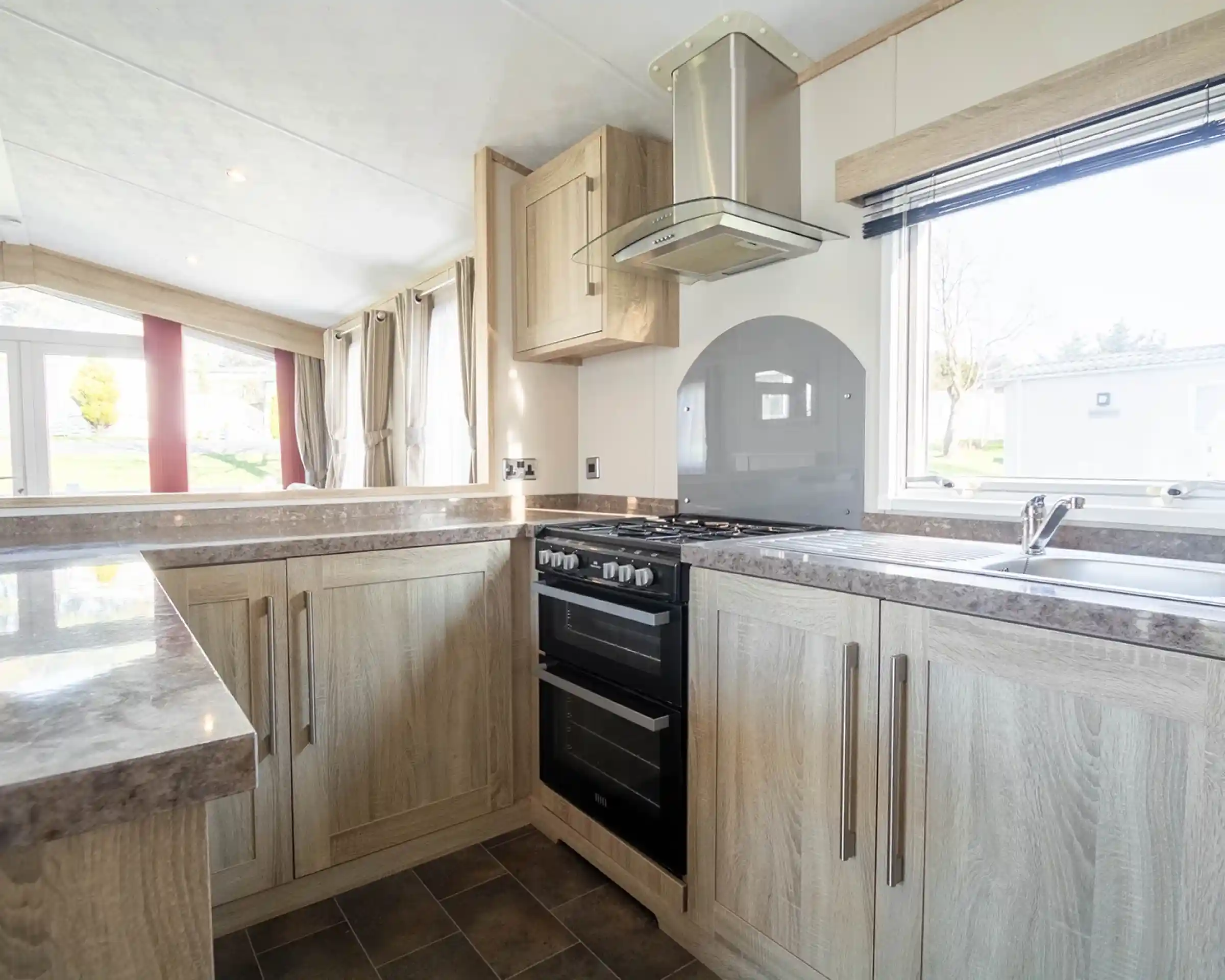 Modern kitchen featuring wooden cabinets, a gas stove, and a sleek countertop. Natural light fills the space through a window, highlighting a contemporary design with neutral tones.