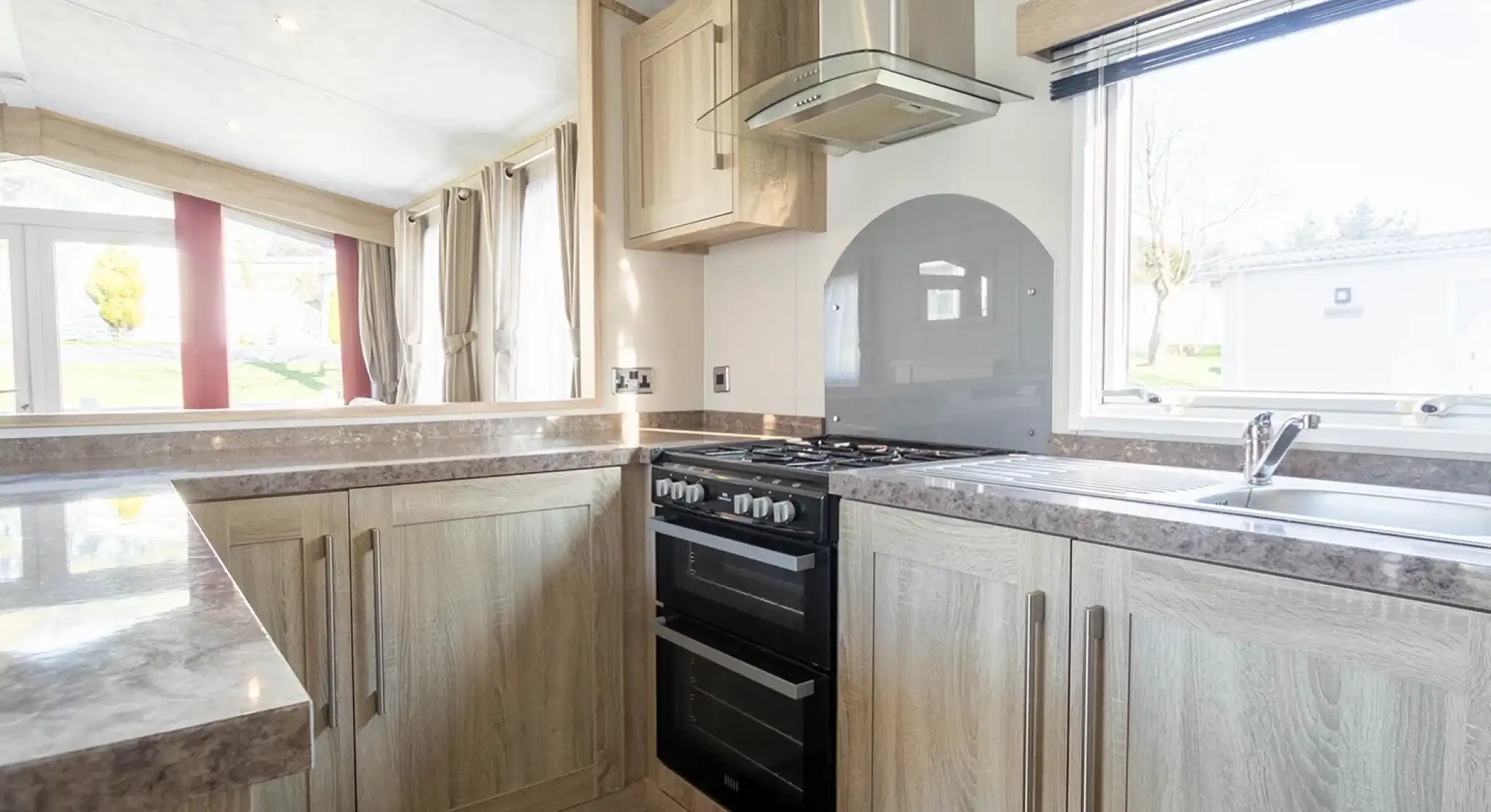 Modern kitchen featuring wooden cabinets, a gas stove, and a sleek countertop. Natural light fills the space through a window, highlighting a contemporary design with neutral tones.