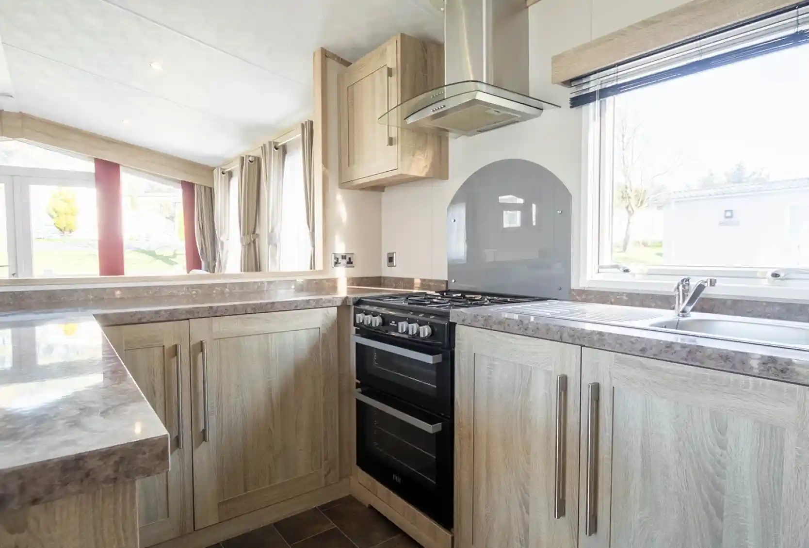 Modern kitchen featuring wooden cabinets, a gas stove, and a sleek countertop. Natural light fills the space through a window, highlighting a contemporary design with neutral tones.