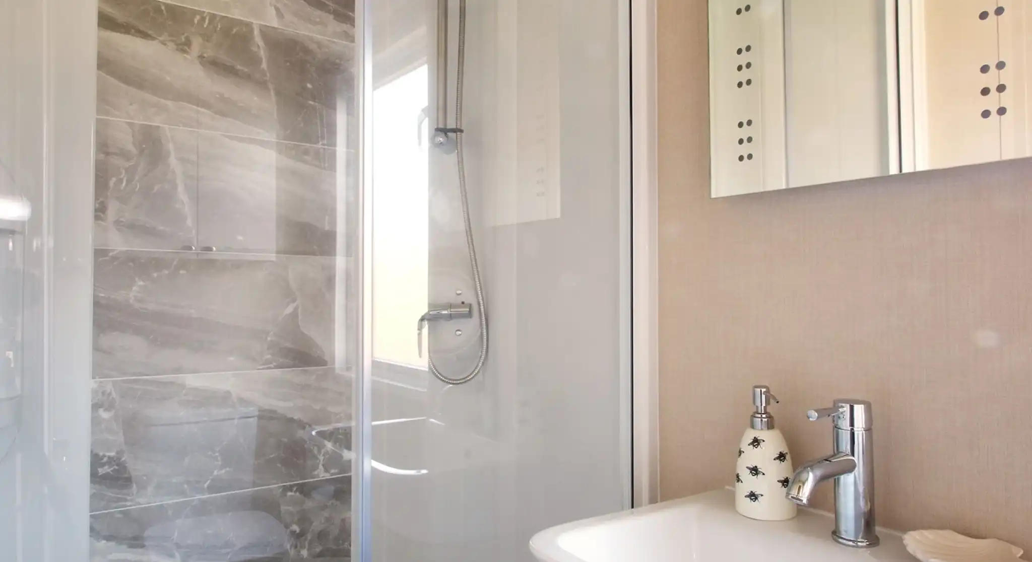 A modern bathroom featuring a glass shower enclosure with a sleek gray tile wall, a white sink with a stylish faucet, and decorative wall elements.