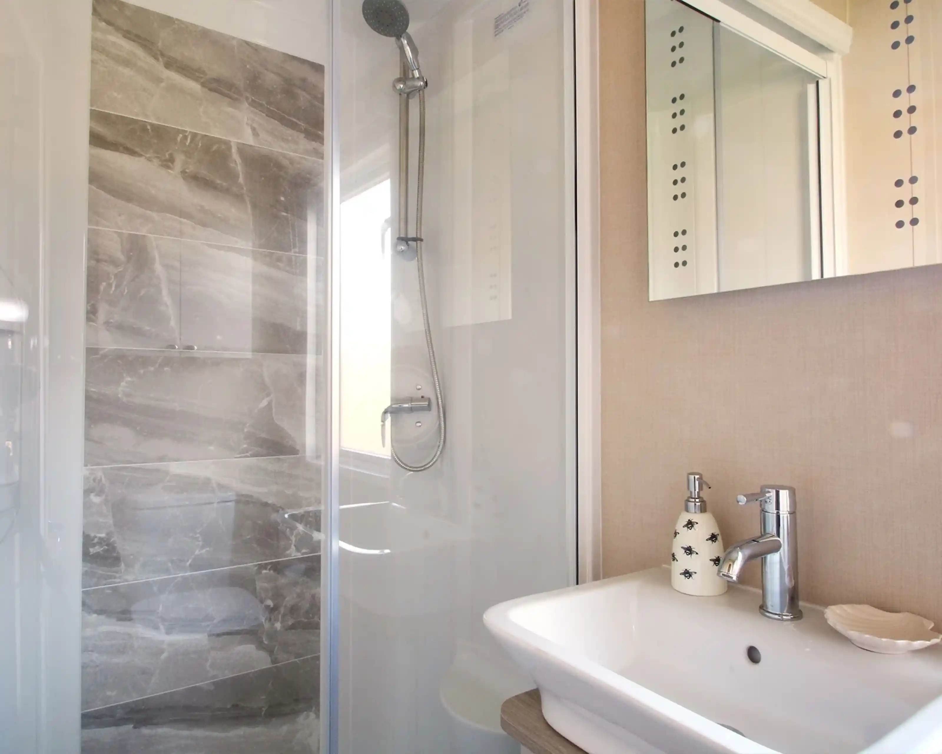 A modern bathroom featuring a glass shower enclosure with a sleek gray tile wall, a white sink with a stylish faucet, and decorative wall elements.