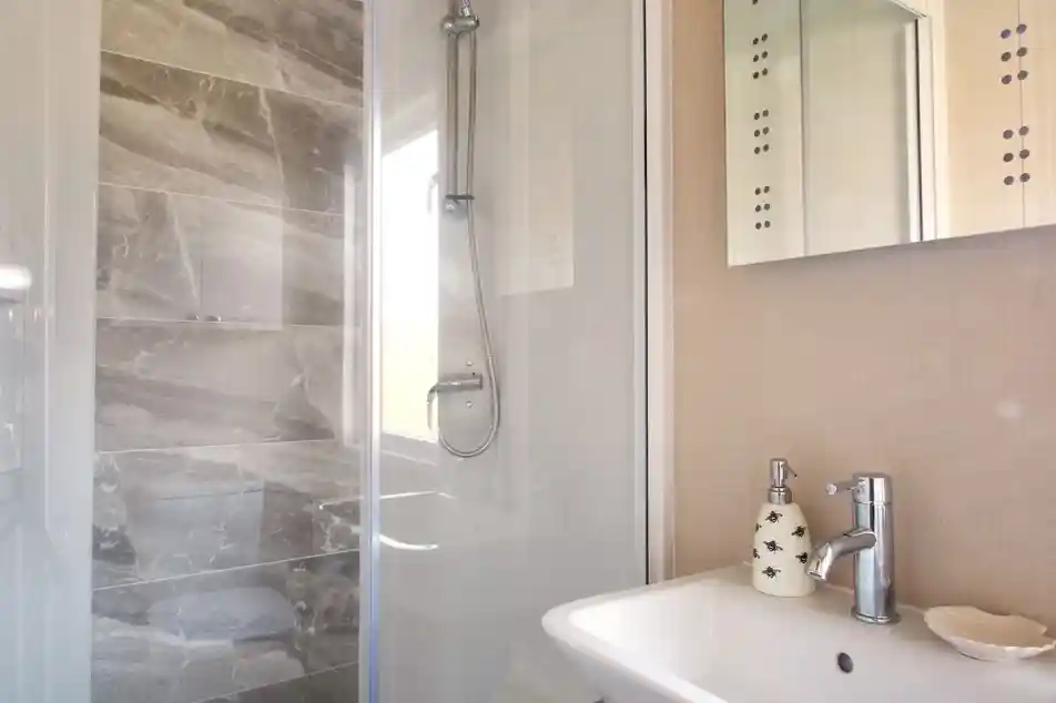 A modern bathroom featuring a glass shower enclosure with a sleek gray tile wall, a white sink with a stylish faucet, and decorative wall elements.
