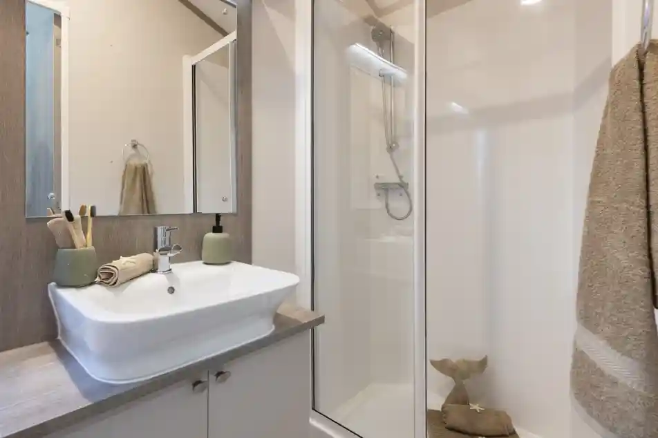 An en suite shower room with shower enclosure, a vanity unit with cupboard under and mirror over, together with a wash basin set onto a wooden work surface. Gold towels and trinkets complete the luxurious feel.