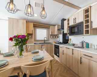 A modern kitchen featuring wooden cabinets and black handles, with herringbone style flooring and a dining table with pendant lighting, creating a warm and inviting atmosphere.
