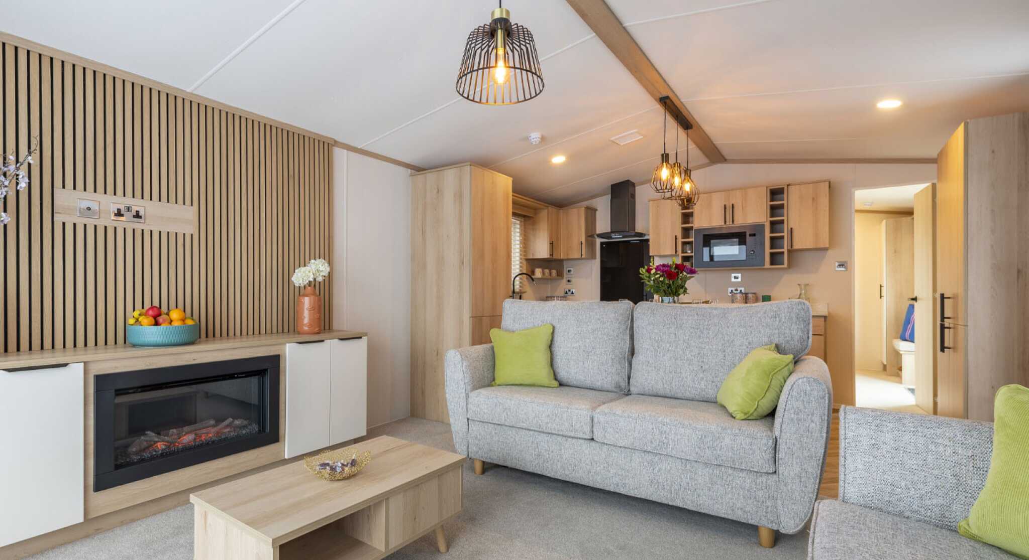 A modern living room showcasing freestanding sofas, a wooden coffee table, and a fireplace built in to a unit with cupboards either side and a feature wooden slatted wall, designed for comfort and socialising.