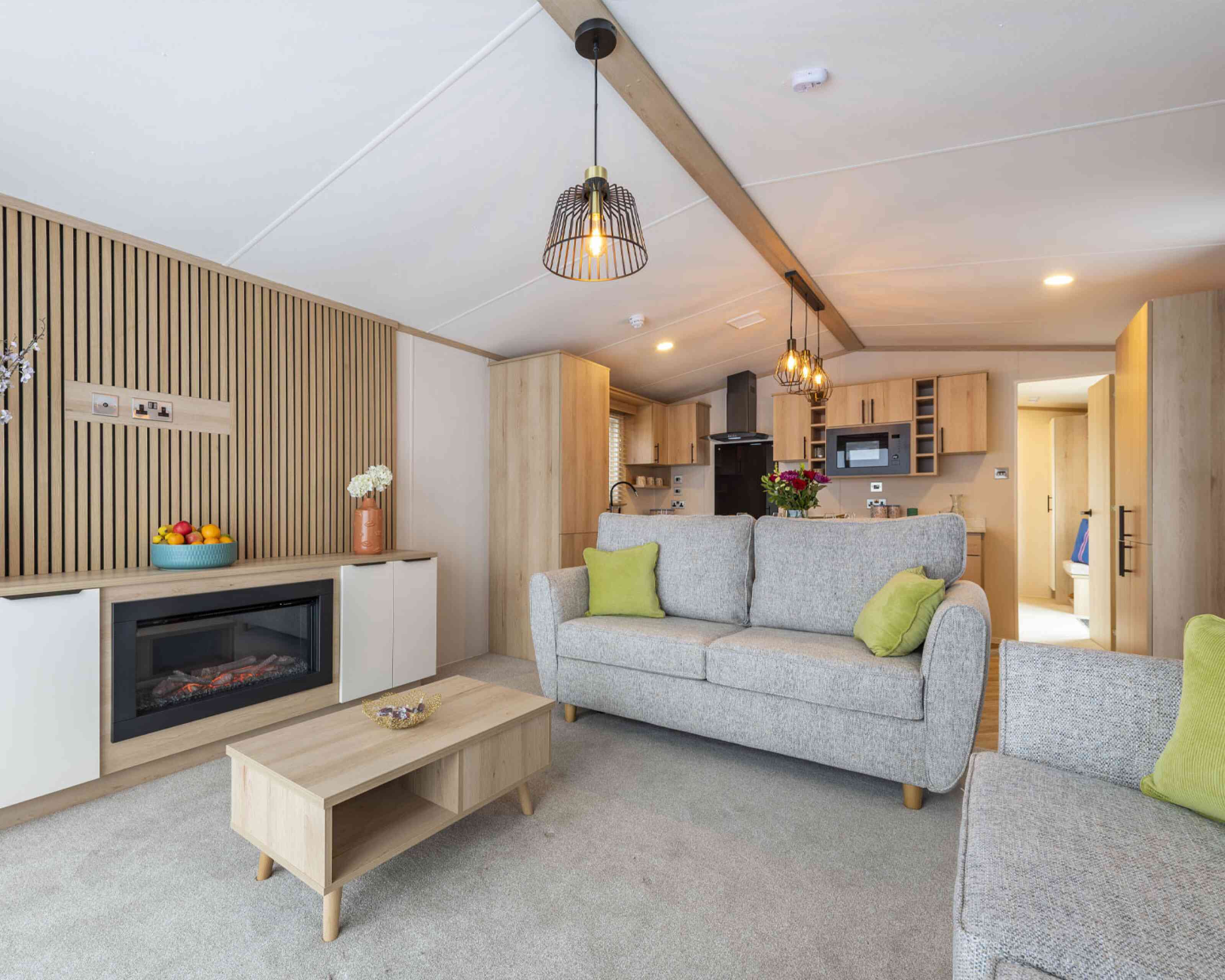 A modern living room showcasing freestanding sofas, a wooden coffee table, and a fireplace built in to a unit with cupboards either side and a feature wooden slatted wall, designed for comfort and socialising.