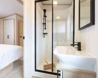 A well-lit en suite bathroom with a stylish shower enclosure and a minimalist sink, designed with neutral tones and elegant finishes.