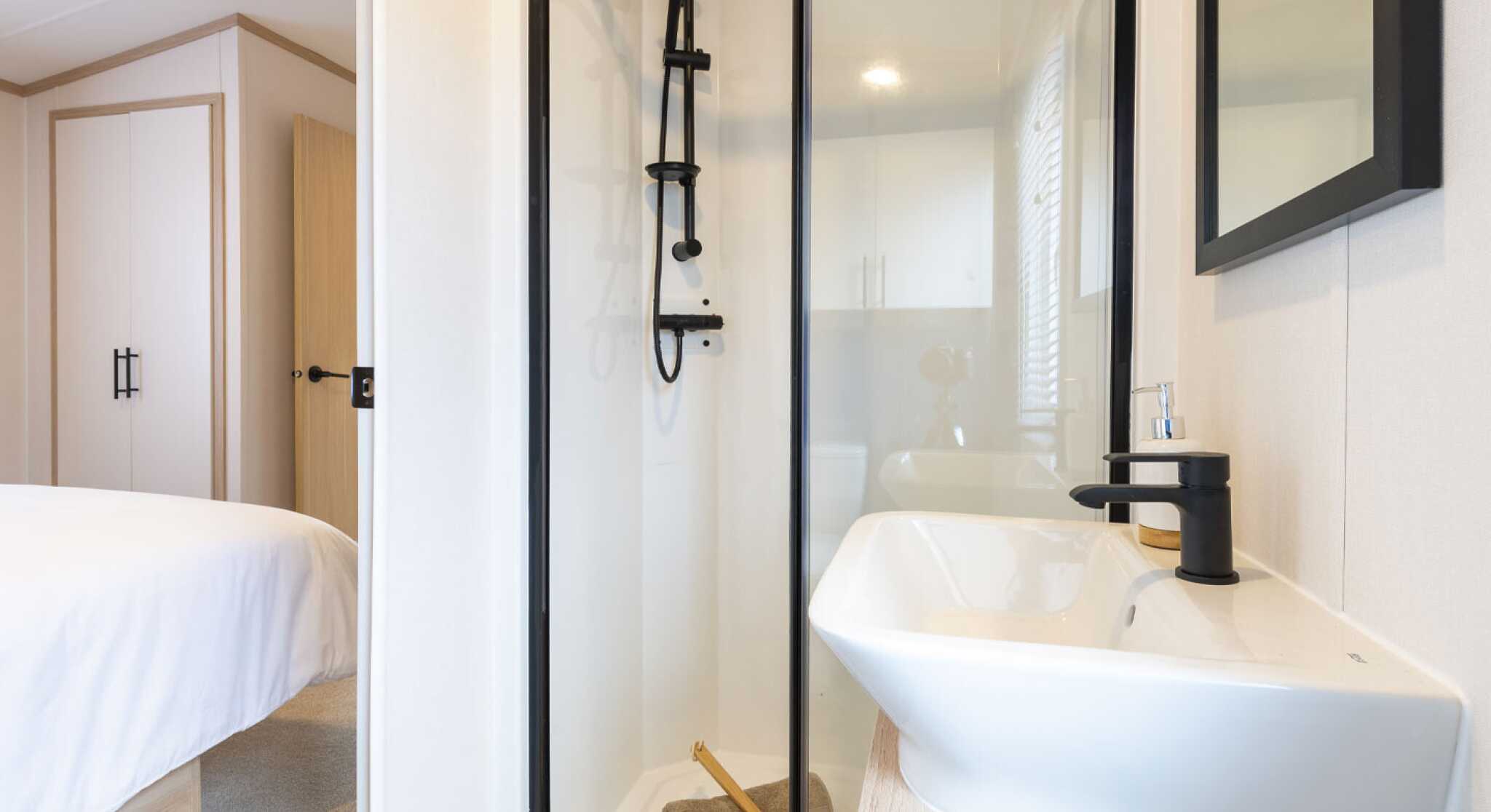 A well-lit en suite bathroom with a stylish shower enclosure and a minimalist sink, designed with neutral tones and elegant finishes.