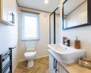A modern bathroom showcasing a sink, toilet, shower enclosure and a mirror, all arranged neatly in a well-lit environment.
