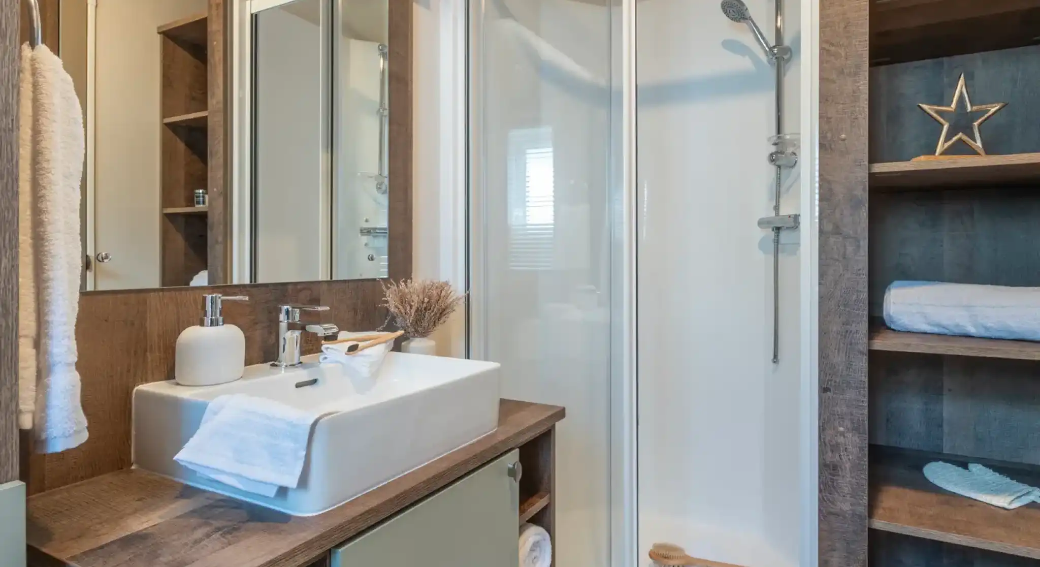 Modern bathroom featuring a glass shower enclosure, a stylish sink with a wooden vanity, and decorative elements like a star and towels. Natural light illuminates the space, enhancing the warm wood tones.
