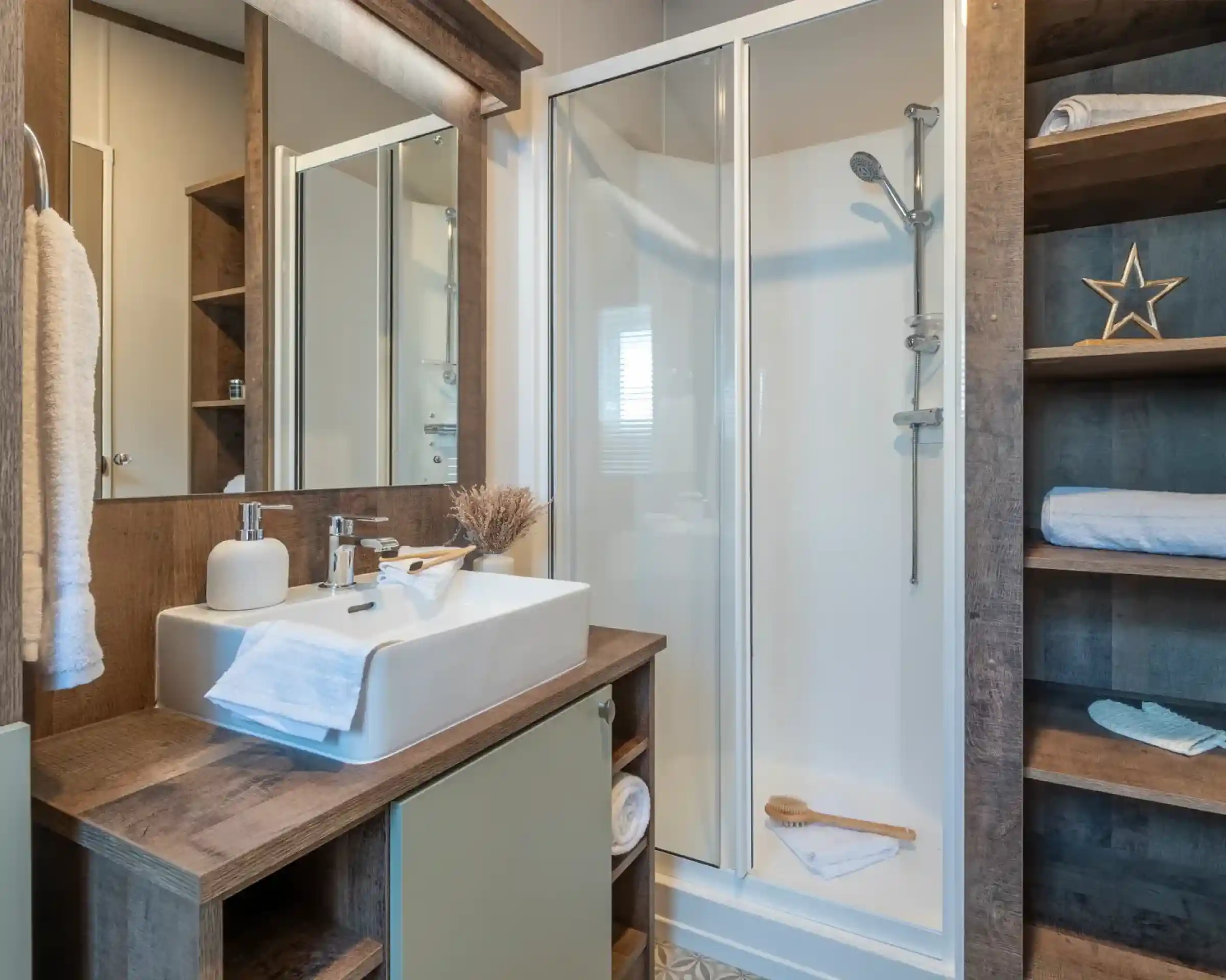 Modern bathroom featuring a glass shower enclosure, a stylish sink with a wooden vanity, and decorative elements like a star and towels. Natural light illuminates the space, enhancing the warm wood tones.