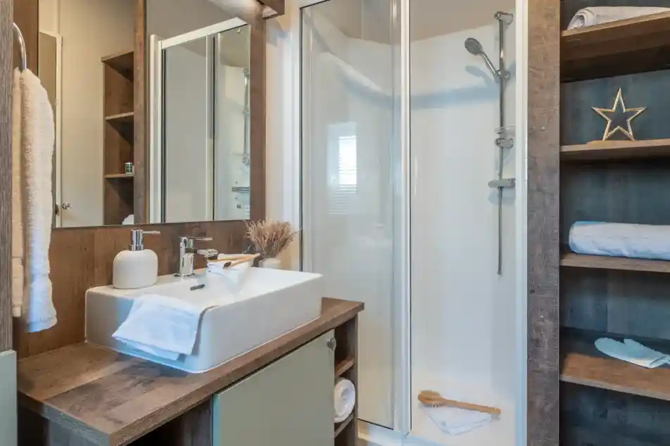 Modern bathroom featuring a glass shower enclosure, a stylish sink with a wooden vanity, and decorative elements like a star and towels. Natural light illuminates the space, enhancing the warm wood tones.
