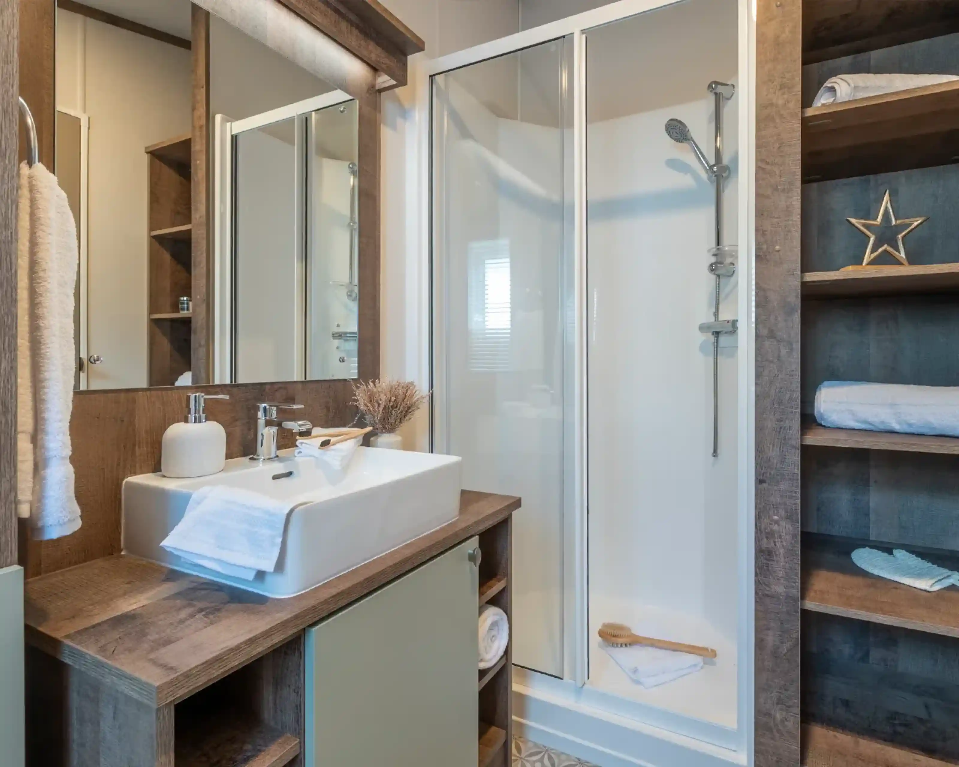 Modern bathroom featuring a glass shower enclosure, a stylish sink with a wooden vanity, and decorative elements like a star and towels. Natural light illuminates the space, enhancing the warm wood tones.