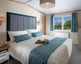 Bright bedroom with a large, neatly made bed featuring blue-patterned accents. A window with matching curtains reveals a scenic garden view. Cosy and inviting atmosphere.