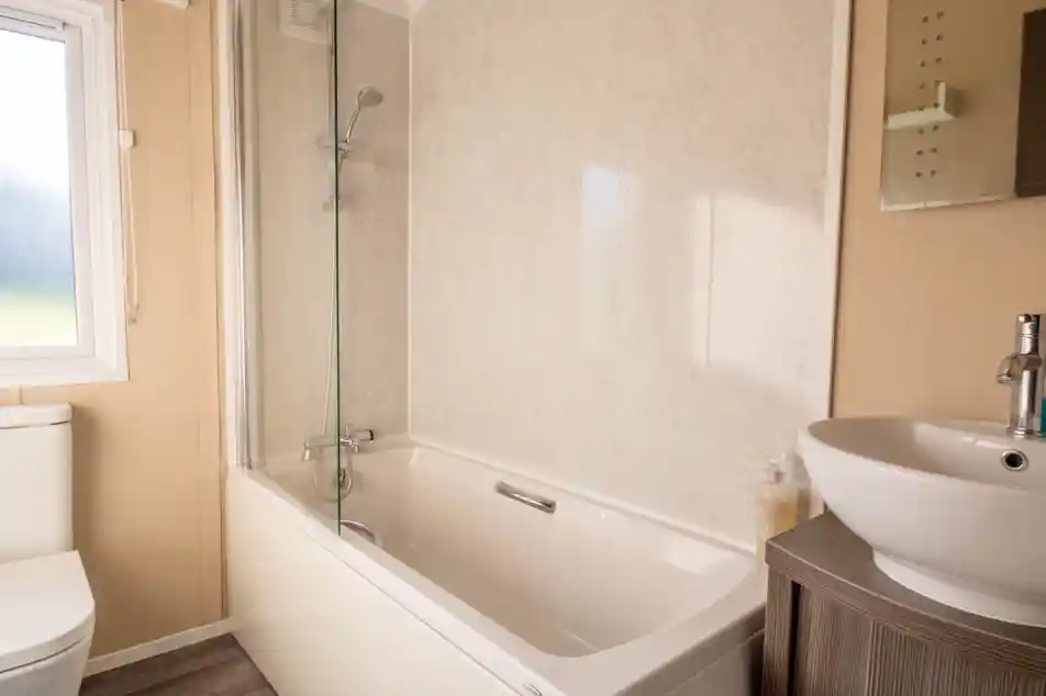 A bathroom with bath with shower over and shower screen, low-level WC and wash basin with vanity unit and mirror.