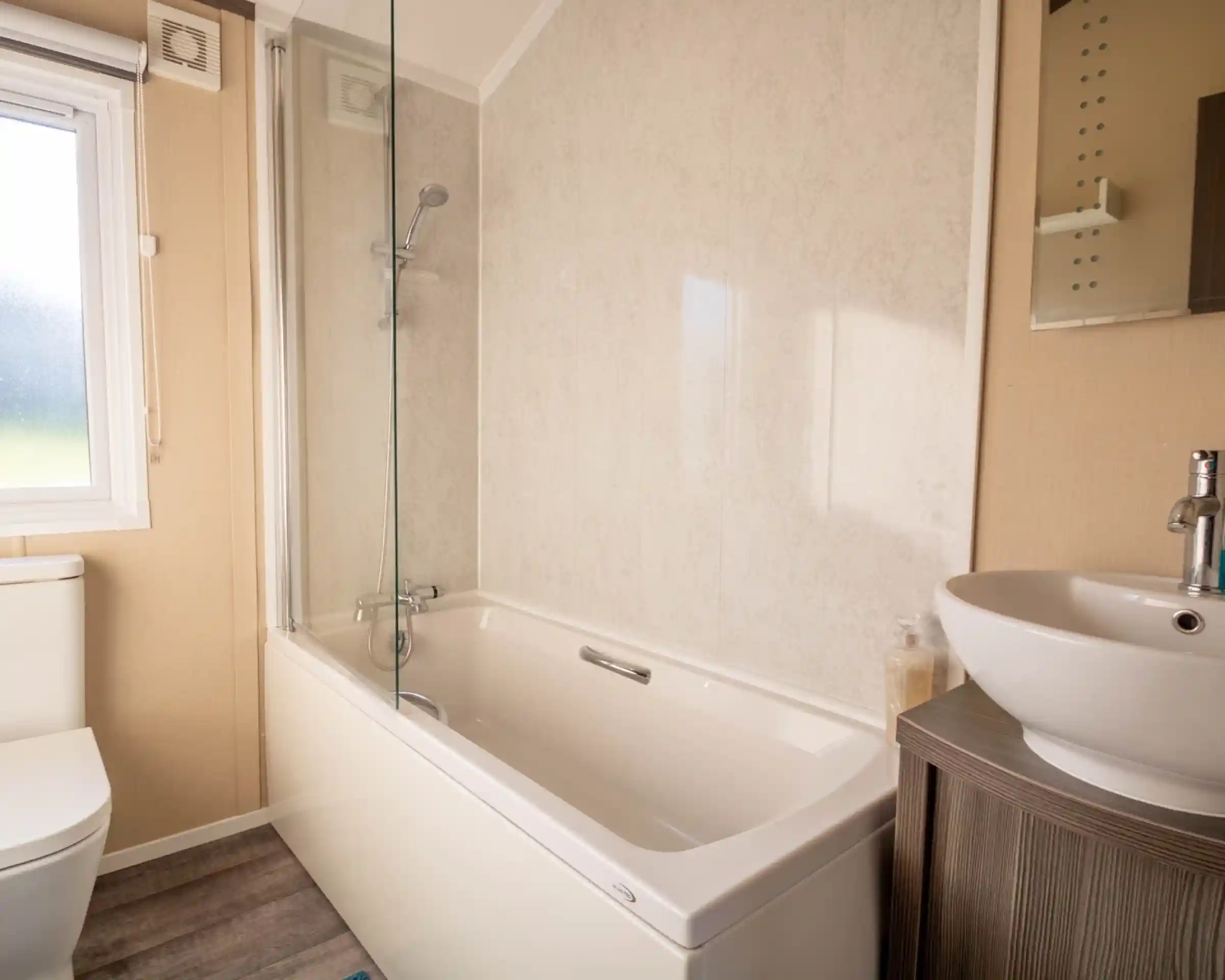 A bathroom with bath with shower over and shower screen, low-level WC and wash basin with vanity unit and mirror.