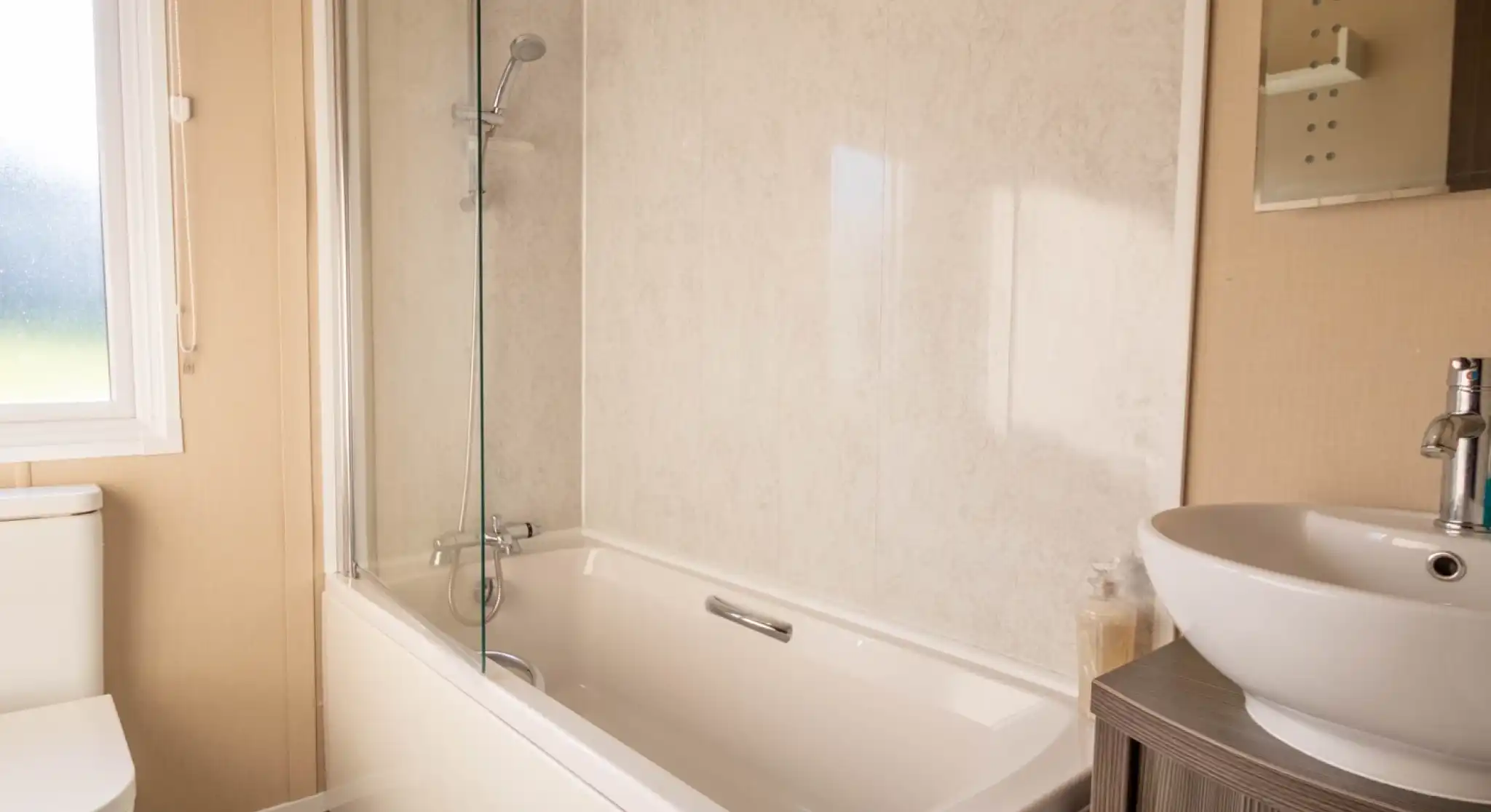 A bathroom with bath with shower over and shower screen, low-level WC and wash basin with vanity unit and mirror.