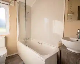 A bathroom with bath with shower over and shower screen, low-level WC and wash basin with vanity unit and mirror.