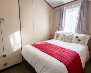 A sweet double bedroom with window behind the double bed with curtains and a wardrobe for storage.
