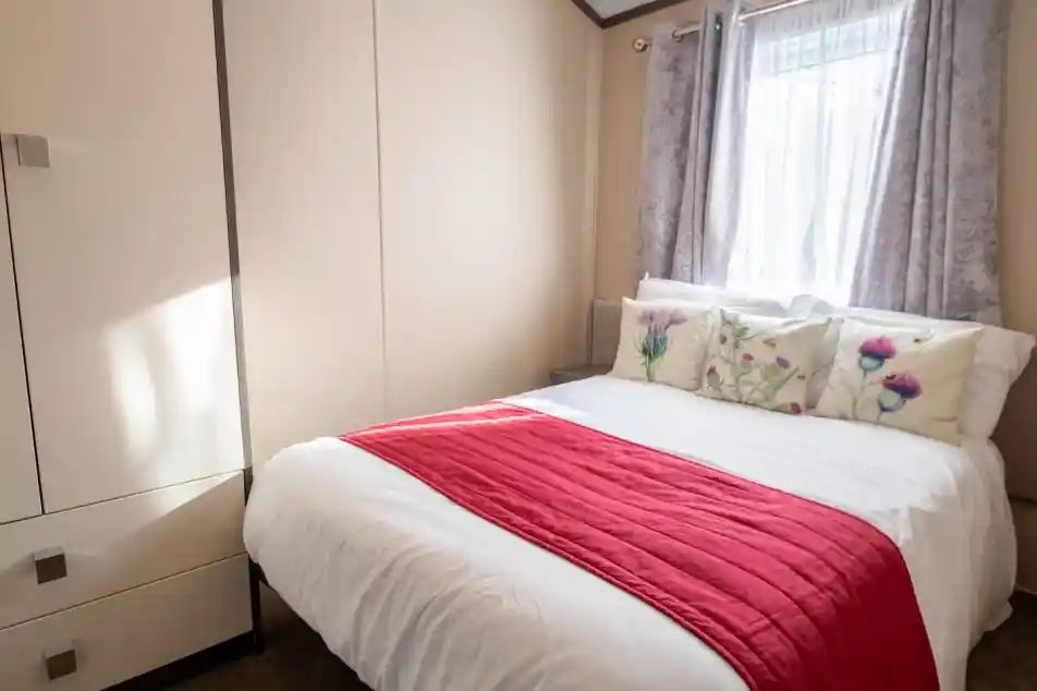 A sweet double bedroom with window behind the double bed with curtains and a wardrobe for storage.