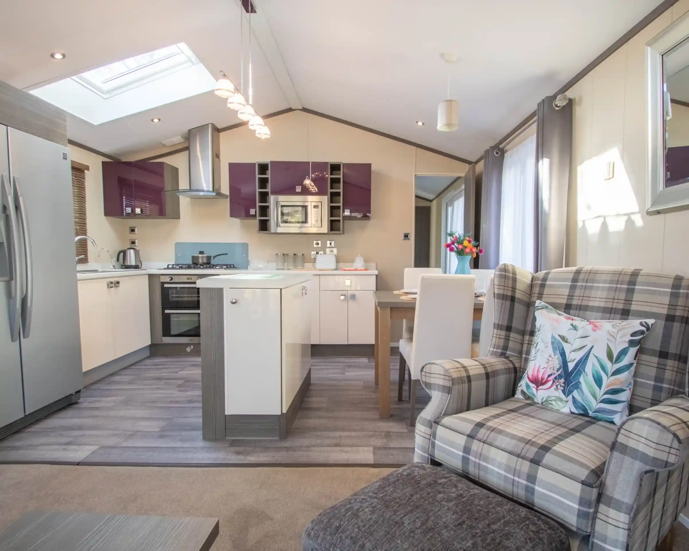 An open plan kitchen, dining, living room with Velux roof window and laminate wood flooring to the kitchen area. A mixture of white gloss and purple gloss cabinets, a kitchen island and a dining table with chairs separates the kitchen area from the lounge.