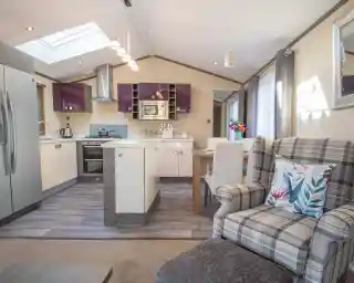 An open plan kitchen, dining, living room with Velux roof window and laminate wood flooring to the kitchen area. A mixture of white gloss and purple gloss cabinets, a kitchen island and a dining table with chairs separates the kitchen area from the lounge.