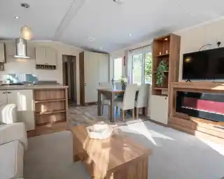 A lounge with coffee table, electric fireplace and TV, with kitchen and dining room in the background.