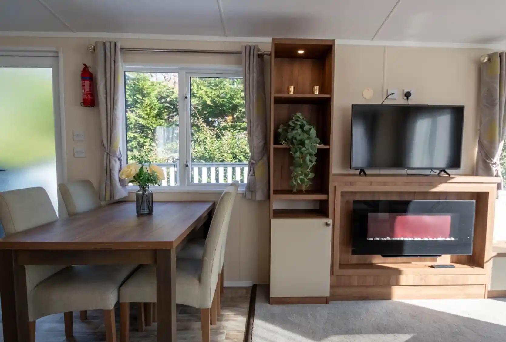A dining area with dining table and chairs leading into a lounge with feature electric fireplace set into cabinets with a TV above.
