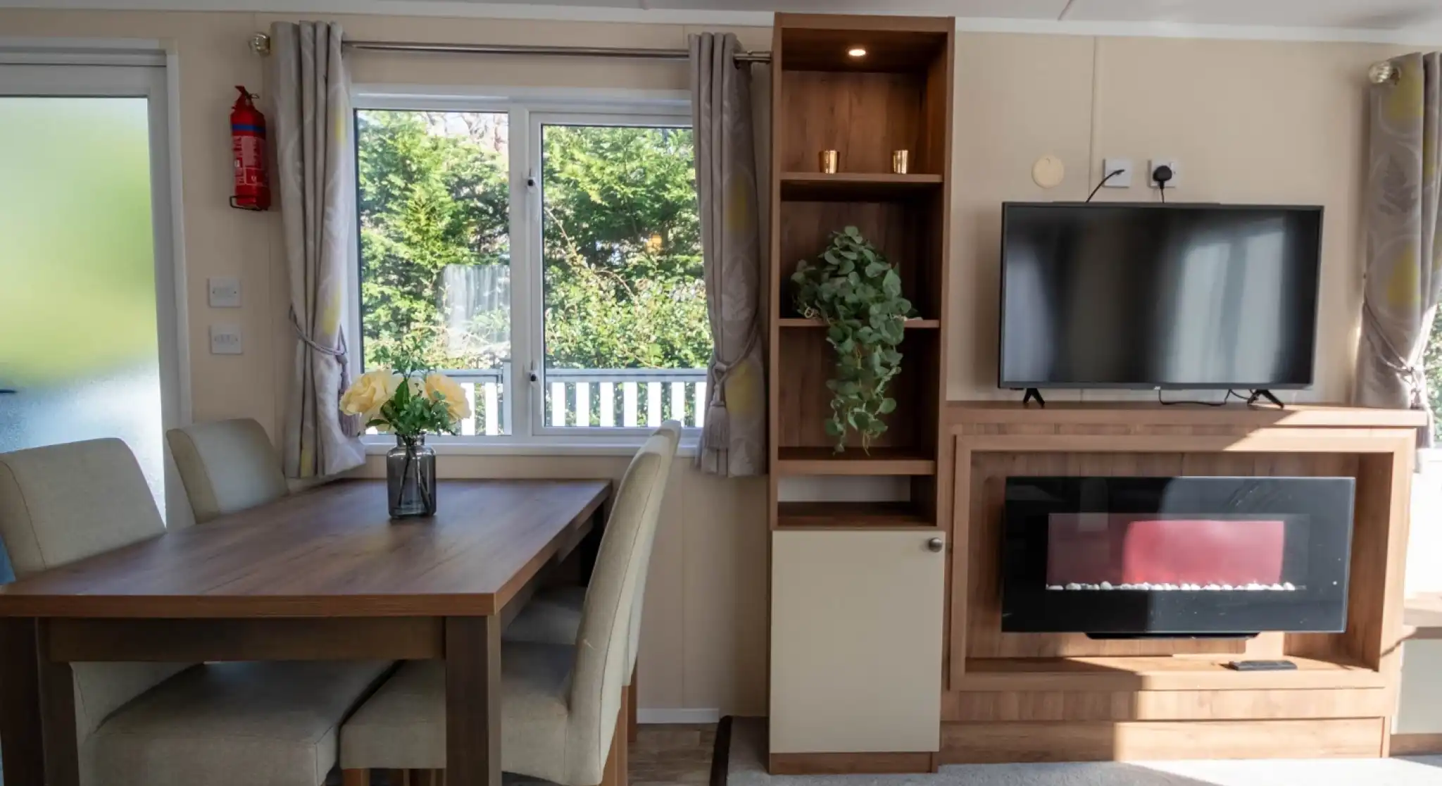 A dining area with dining table and chairs leading into a lounge with feature electric fireplace set into cabinets with a TV above.