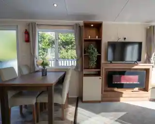 A dining area with dining table and chairs leading into a lounge with feature electric fireplace set into cabinets with a TV above.