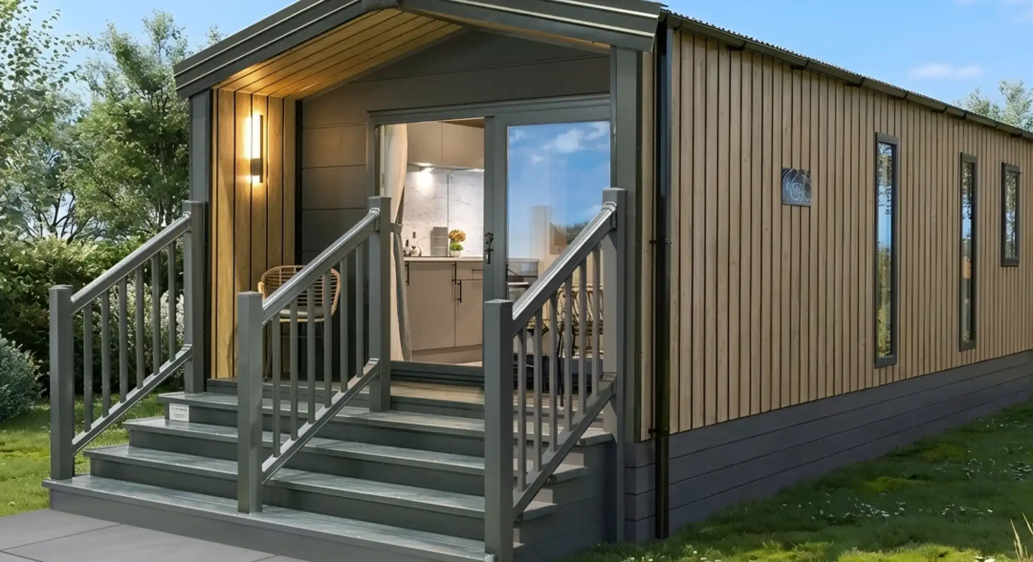 A modern, wooden-clad cabin with a slanted roof, featuring a welcoming front porch with steps. The cabin has large windows, allowing natural light to enter, and is surrounded by greenery.