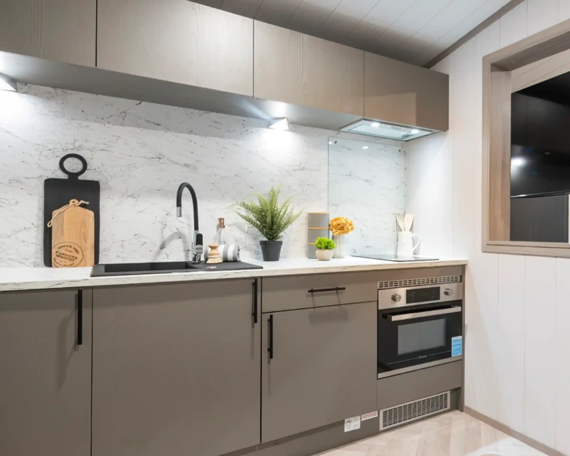 Modern kitchen featuring sleek gray cabinetry, a marble backsplash, and stainless steel appliances. A decorative plant and yellow flowers add a touch of color, along with kitchen utensils and a cutting board displayed on the counter.