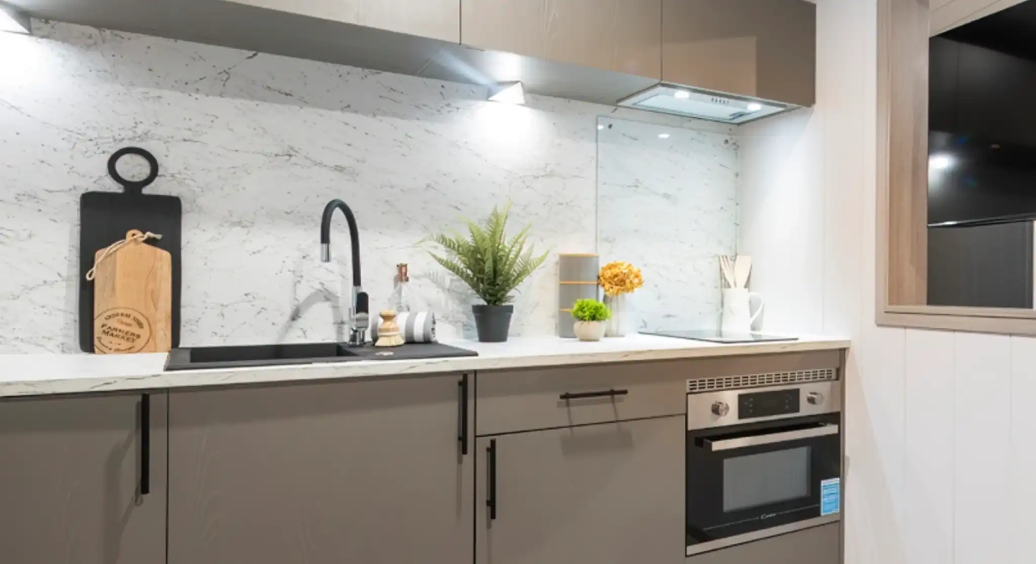 Modern kitchen featuring sleek gray cabinetry, a marble backsplash, and stainless steel appliances. A decorative plant and yellow flowers add a touch of color, along with kitchen utensils and a cutting board displayed on the counter.