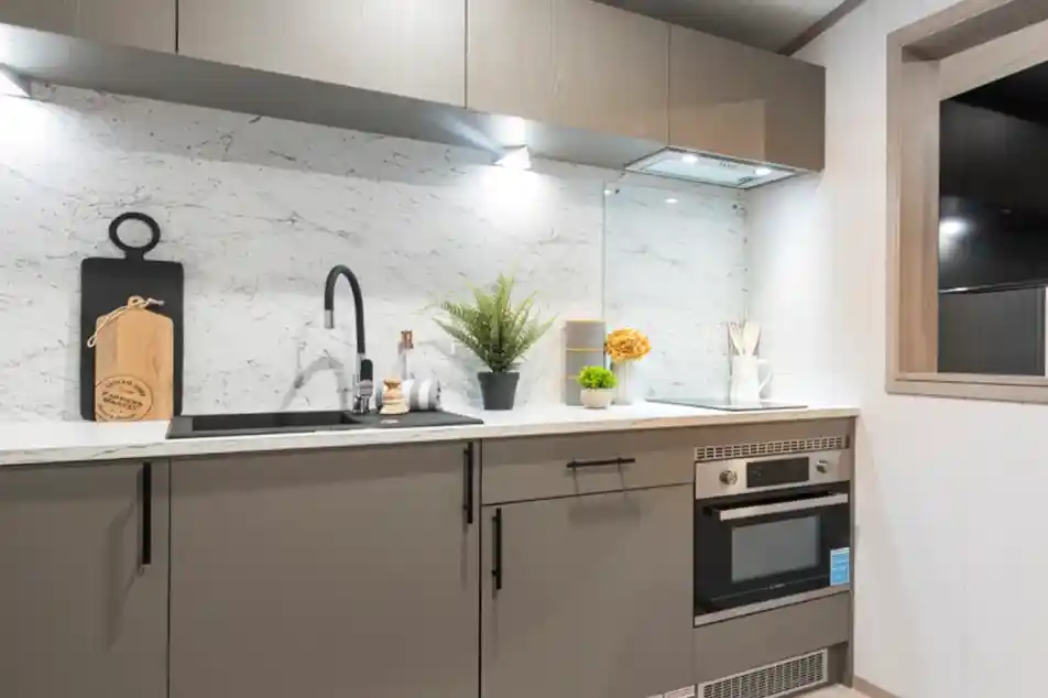 Modern kitchen featuring sleek gray cabinetry, a marble backsplash, and stainless steel appliances. A decorative plant and yellow flowers add a touch of color, along with kitchen utensils and a cutting board displayed on the counter.