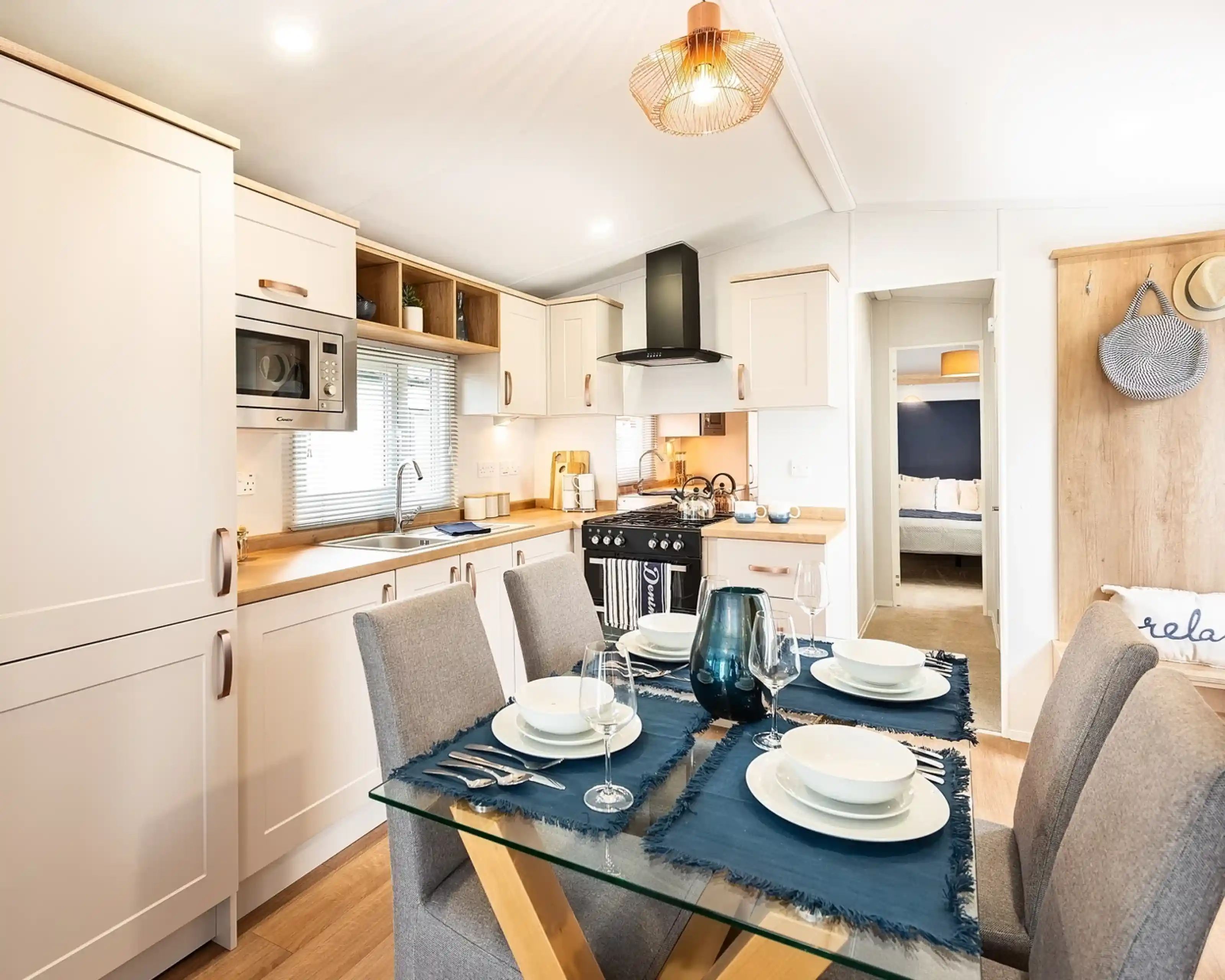 A modern kitchen dining room complete with a range of cream cabinetry including an oven with gas hob and extractor over, a stainless steel sink unit and a dining table set for four.