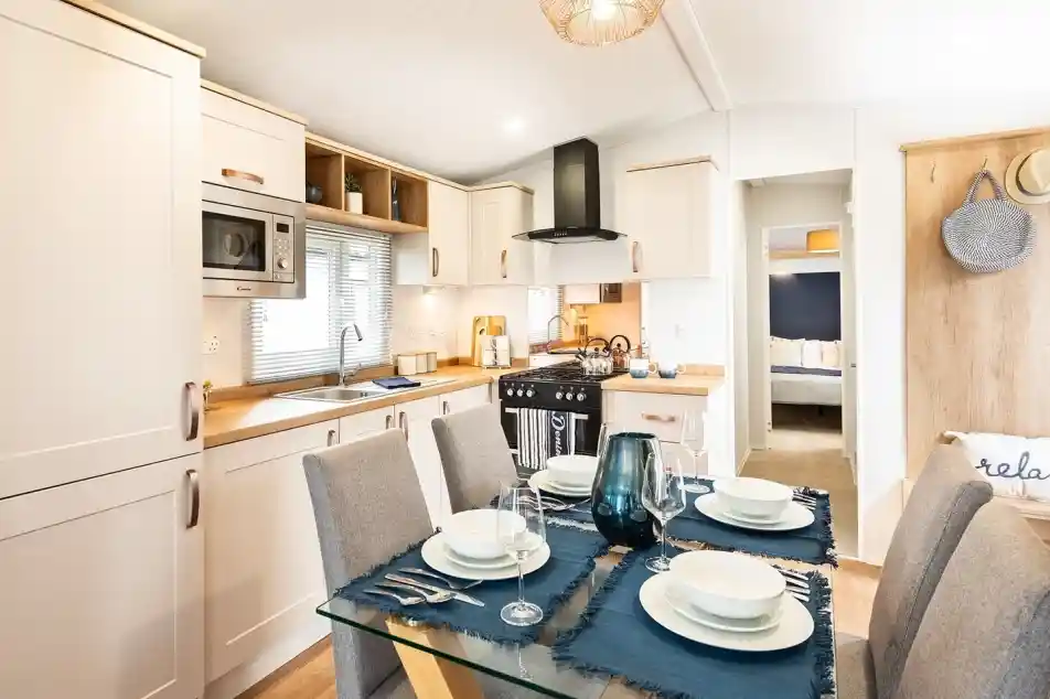 A modern kitchen dining room complete with a range of cream cabinetry including an oven with gas hob and extractor over, a stainless steel sink unit and a dining table set for four.
