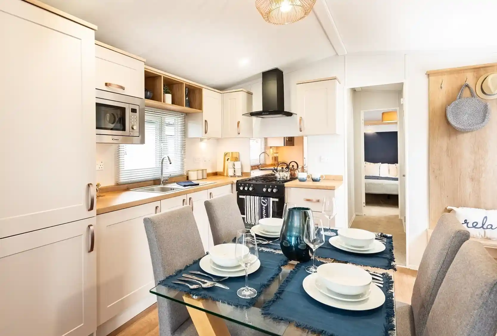 A modern kitchen dining room complete with a range of cream cabinetry including an oven with gas hob and extractor over, a stainless steel sink unit and a dining table set for four.