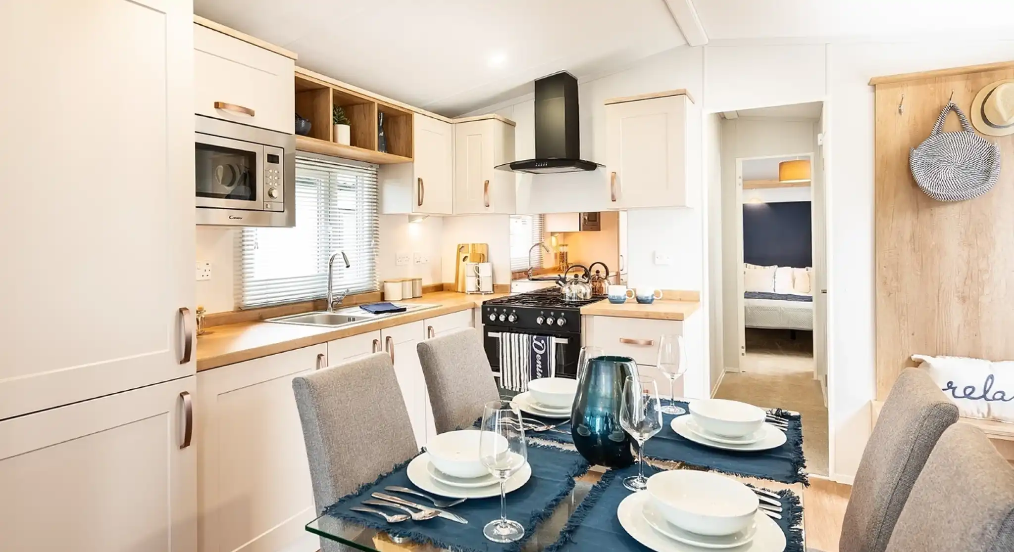 A modern kitchen dining room complete with a range of cream cabinetry including an oven with gas hob and extractor over, a stainless steel sink unit and a dining table set for four.