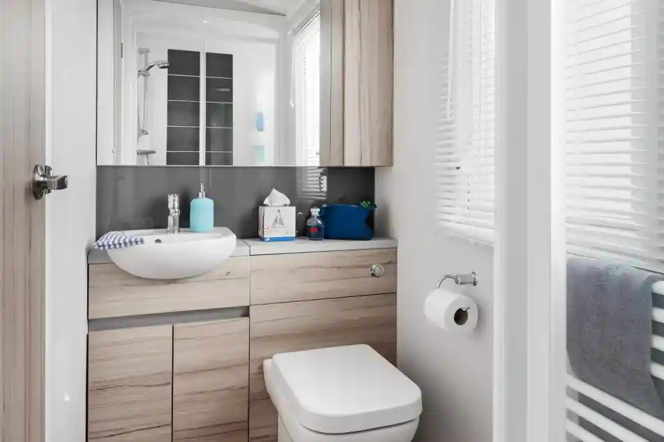 Modern bathroom with a white vessel sink, light wood vanity, and toilet next to a window with blinds.