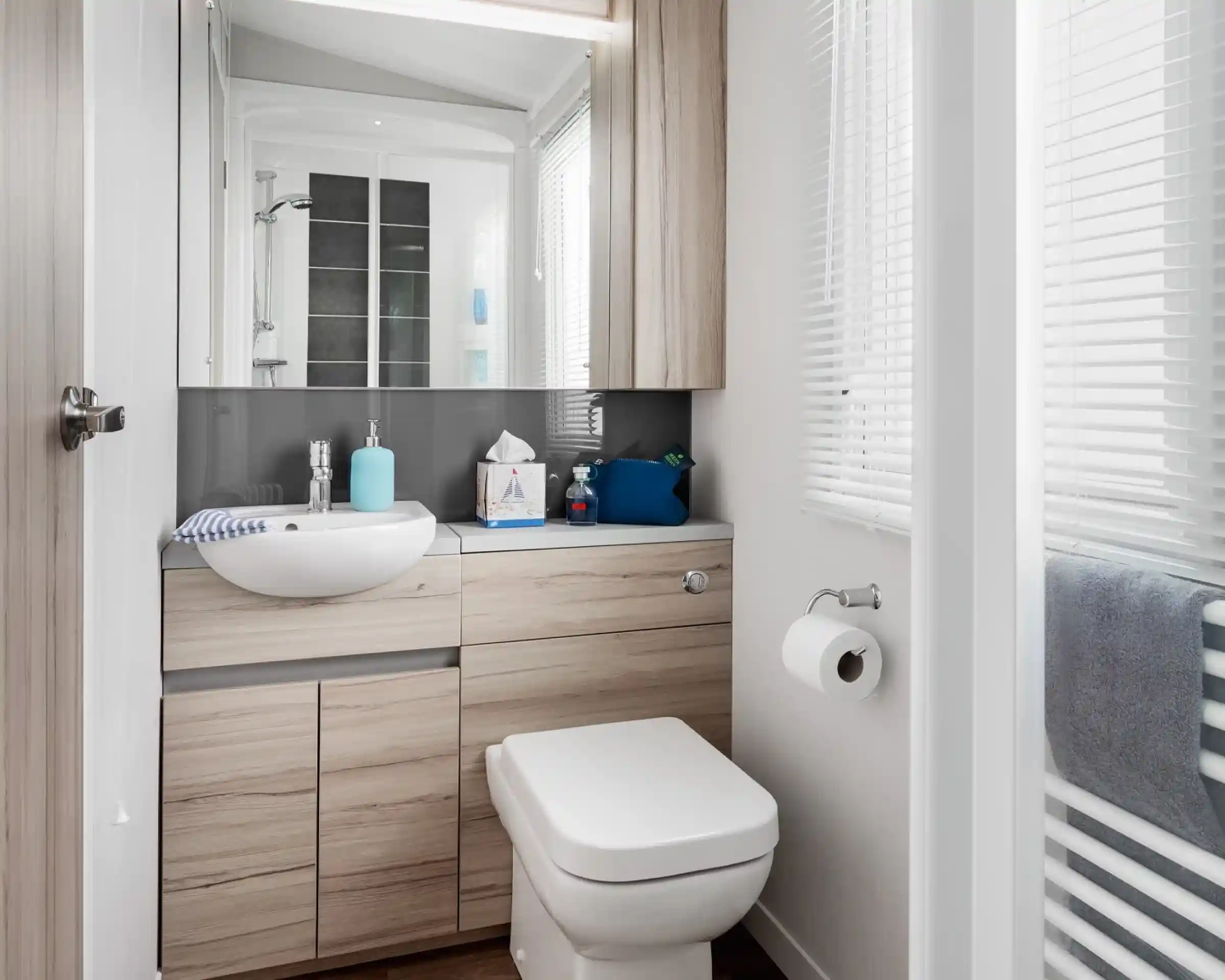 Modern bathroom with a white vessel sink, light wood vanity, and toilet next to a window with blinds.